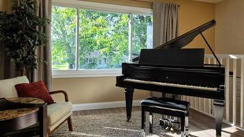 A room with a grand piano, a sofa, a window with curtains, and a plant.