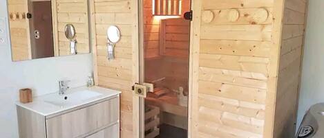 Un baño tipo cabaña de madera con lavamanos, espejo y puerta que da a una zona de ducha.