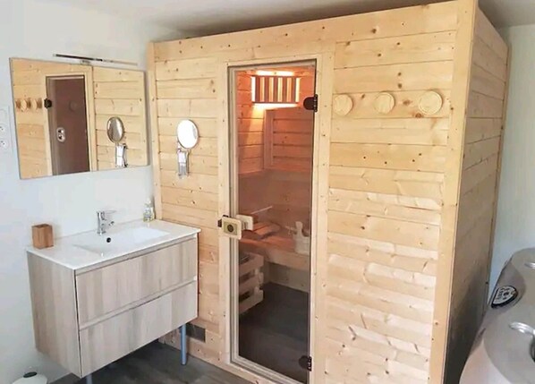 A wooden cabin-style bathroom with a sink, mirror, and a door leading to a shower area.
