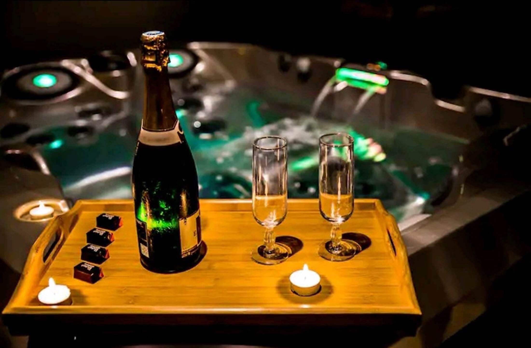 A wooden tray with a bottle and two glasses, a candle, and a lit burner on a table.