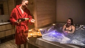 Un hombre con una bata roja sirve champán en una bañera de hidromasaje donde una mujer está sentada.