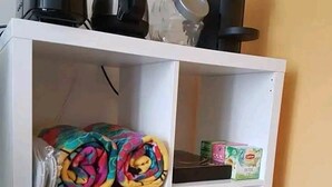 Un estante blanco con varios objetos, incluyendo una manta colorida, una caja y un pequeño recipiente.