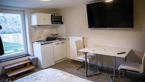 Una habitación compacta con kitchenette, una cama, un televisor y un ventanal.