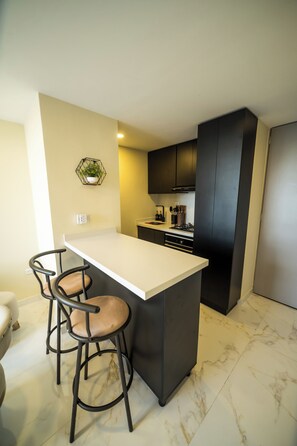 Una cocina moderna con una isla central, taburetes de bar, armarios oscuros y piso de mármol.