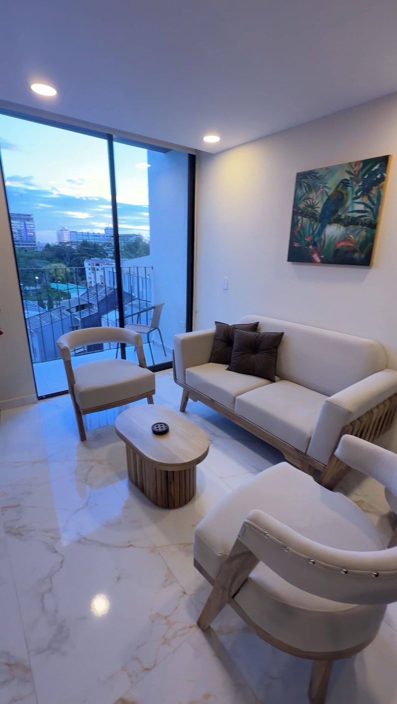 Un salon moderne comprenant un canapé, deux fauteuils, une table basse et une grande fenêtre donnant sur la ville.