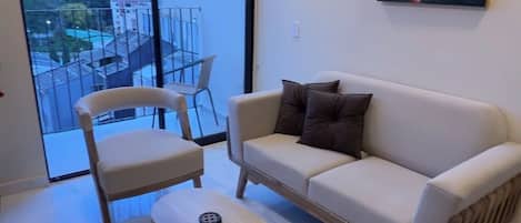A modern living room with a sofa, two armchairs, a coffee table, and a large window offering a city view.