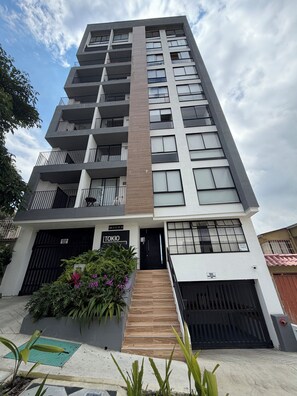 Un moderno edificio residencial de varios pisos con balcones, una entrada con reja y una escalera que conduce a la entrada.