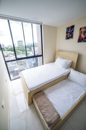 Un dormitorio con un ventanal grande, una cama con ropa de cama blanca y dos cuadros en la pared.