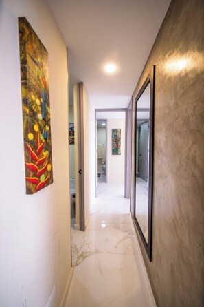 A hallway with a marble floor, a painting on the left wall, and a mirror on the right.