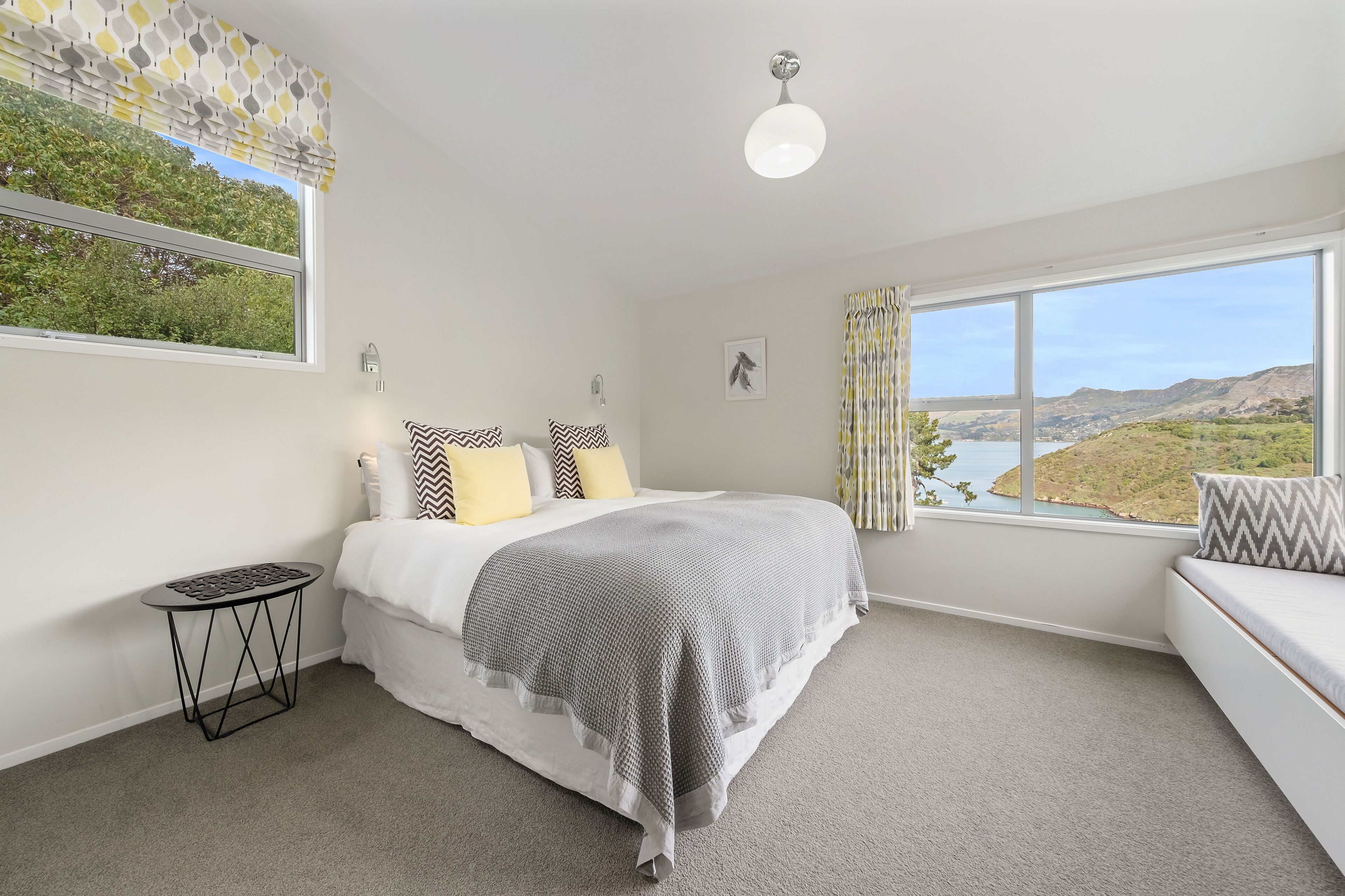 A bedroom with a bed, bedside table, and a view of a landscape through a window.