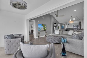 A modern living room with a grey sofa, a tufted armchair, a glass coffee table, and a flat-screen TV. - Top-Floor Coastal Escape | Bay Views | Naples Retreat (Naples)