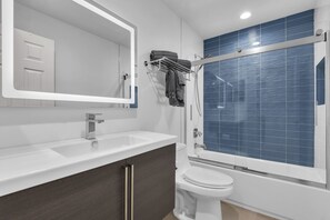 Un baño moderno con un lavamanos blanco, armarios de madera oscura, un inodoro blanco y un box de ducha con azulejos azules.