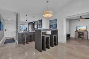 Une cuisine moderne avec des meubles de couleur sombre, un îlot central, des luminaires suspendus et une vue sur l’extérieur.