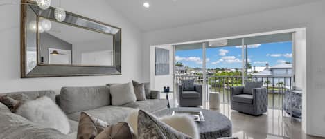 A modern living room with a large sofa, a ceiling fan, and a view of a body of water through large glass doors.
