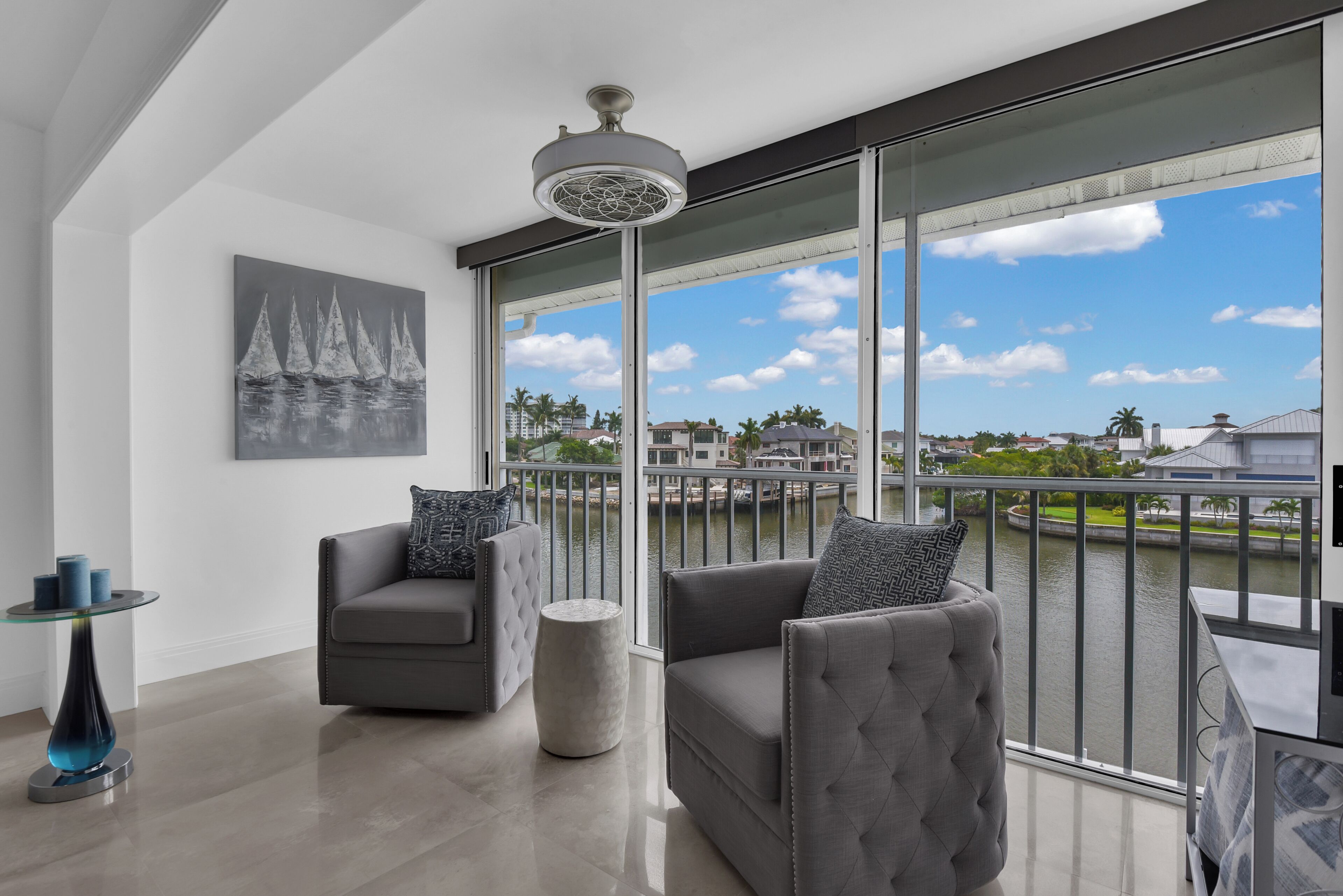 Un balcon moderne offrant une vue sur une rivière et des bâtiments éloignés, aménagé avec deux fauteuils gris et une petite table.