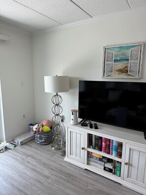 A living room with a flat-screen TV, a lamp, a bookshelf, and a painting on the wall. - Tranquil 1-bedroom condo with AC in Ocean City (Ocean City)