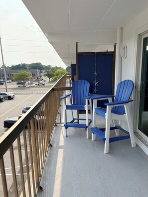 Un balcon avec une table et des chaises, une vue sur la rue et une porte décorée de motifs d’étoiles de mer.