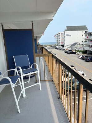 A balcony with blue chairs, a view of a parking lot, and a building labeled 'Ocean Harbour'. - Tranquil 1-bedroom condo with AC in Ocean City (Ocean City)