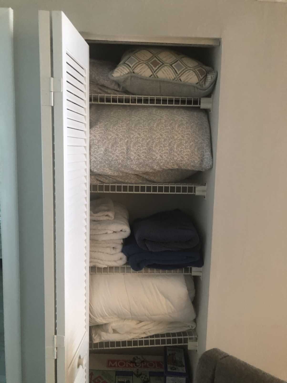 A closet with shelves containing folded towels and a pillow.