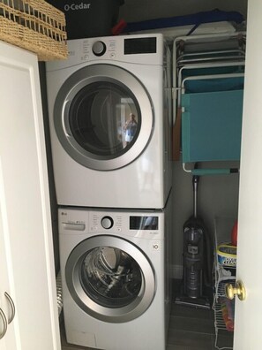 A laundry area with two stacked washing machines, a blue storage unit, and a vacuum cleaner. - Indian River Plantation beautiful condo on Hutchinson Island  steps to the beach (Stuart)