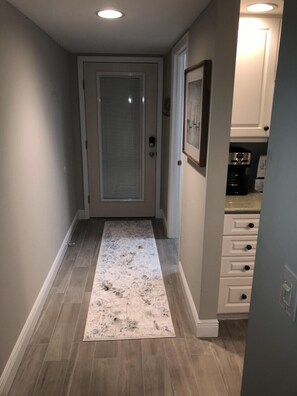 A hallway with a patterned rug, a door with a frosted glass panel, and a kitchen area with cabinets and appliances. - Indian River Plantation beautiful condo on Hutchinson Island  steps to the beach (Stuart)