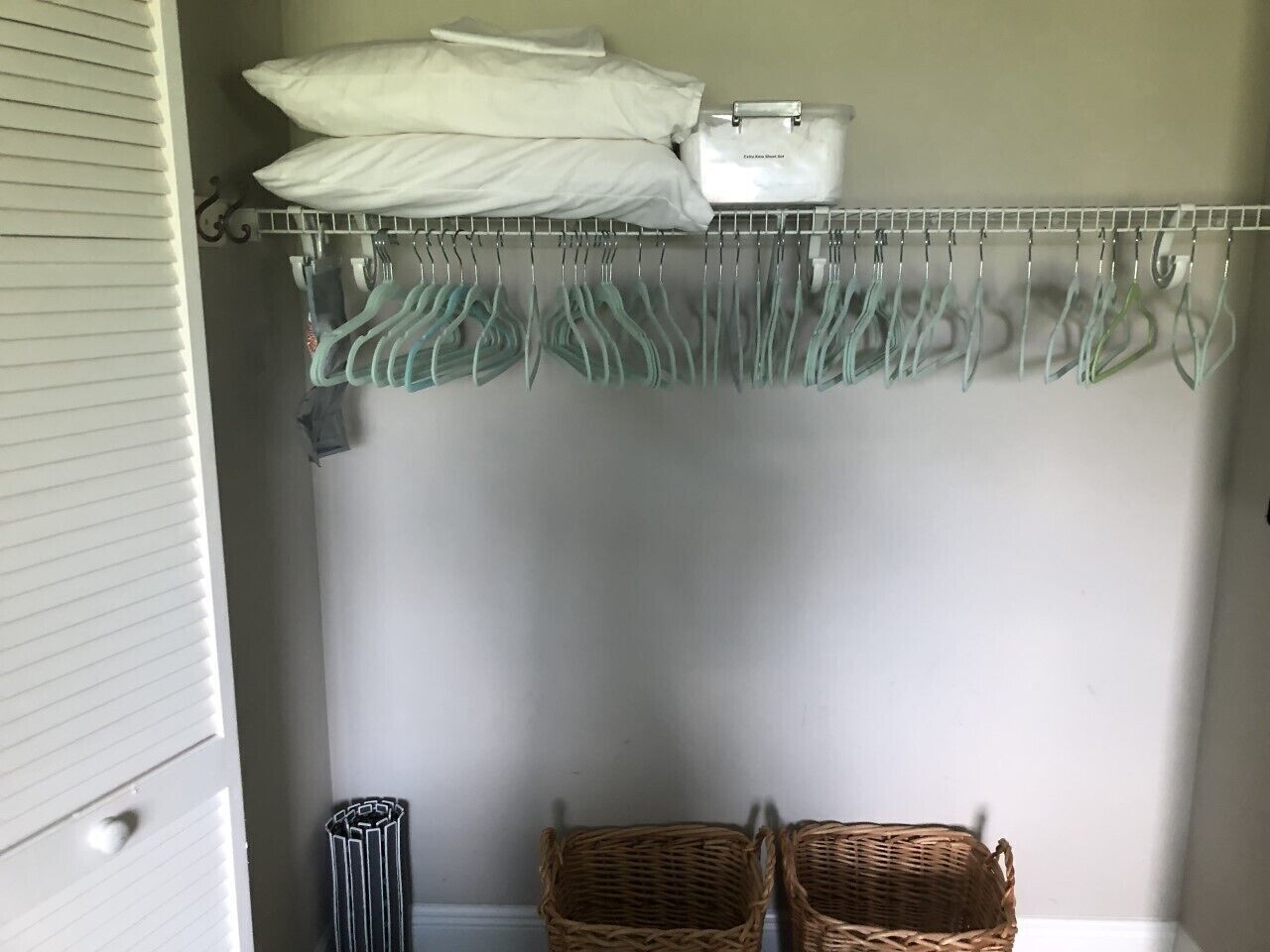 A closet with hanging clothes, a white storage box, and two baskets.