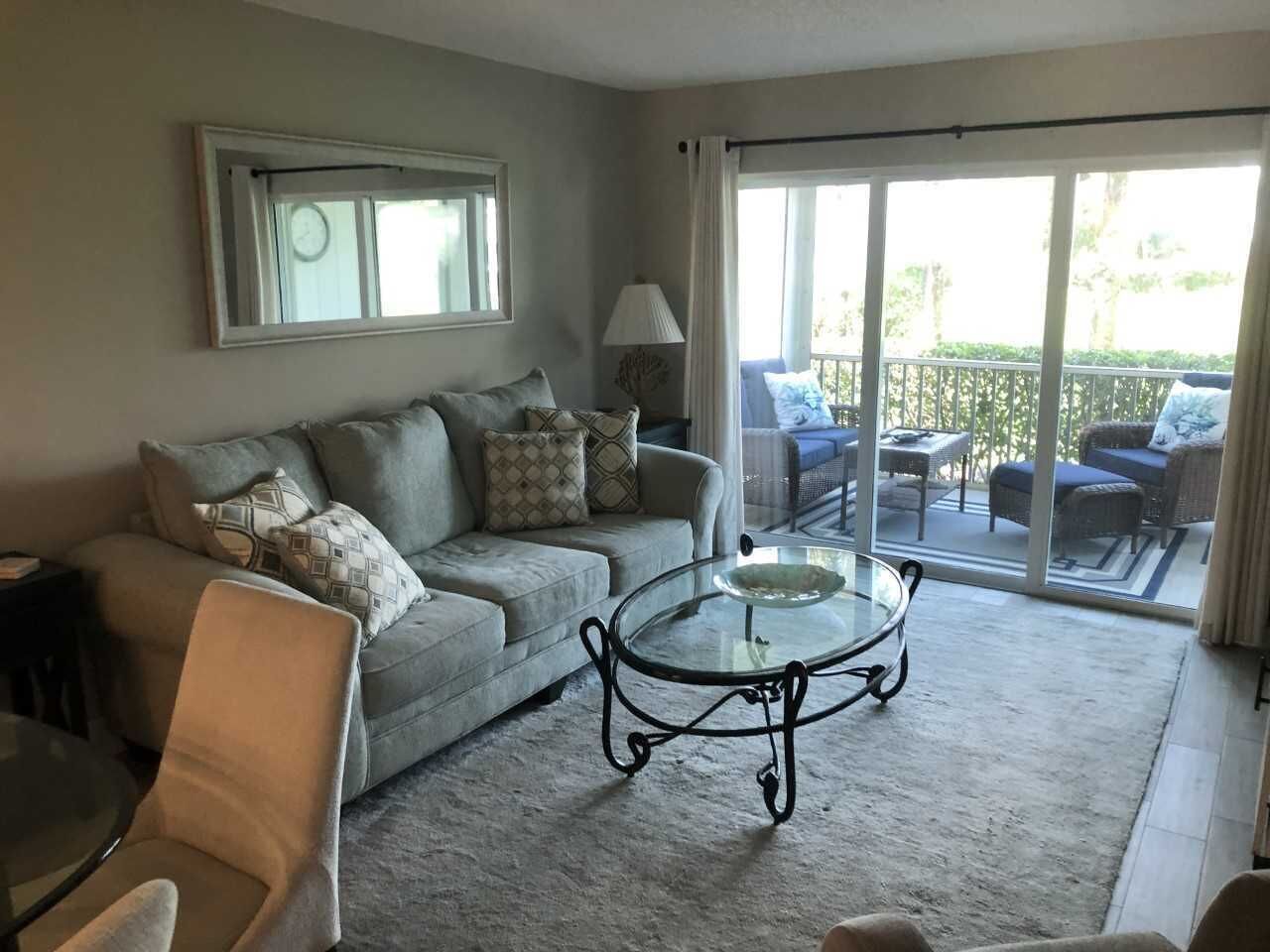A living room with a sofa, a glass coffee table, and a view of an outdoor balcony.