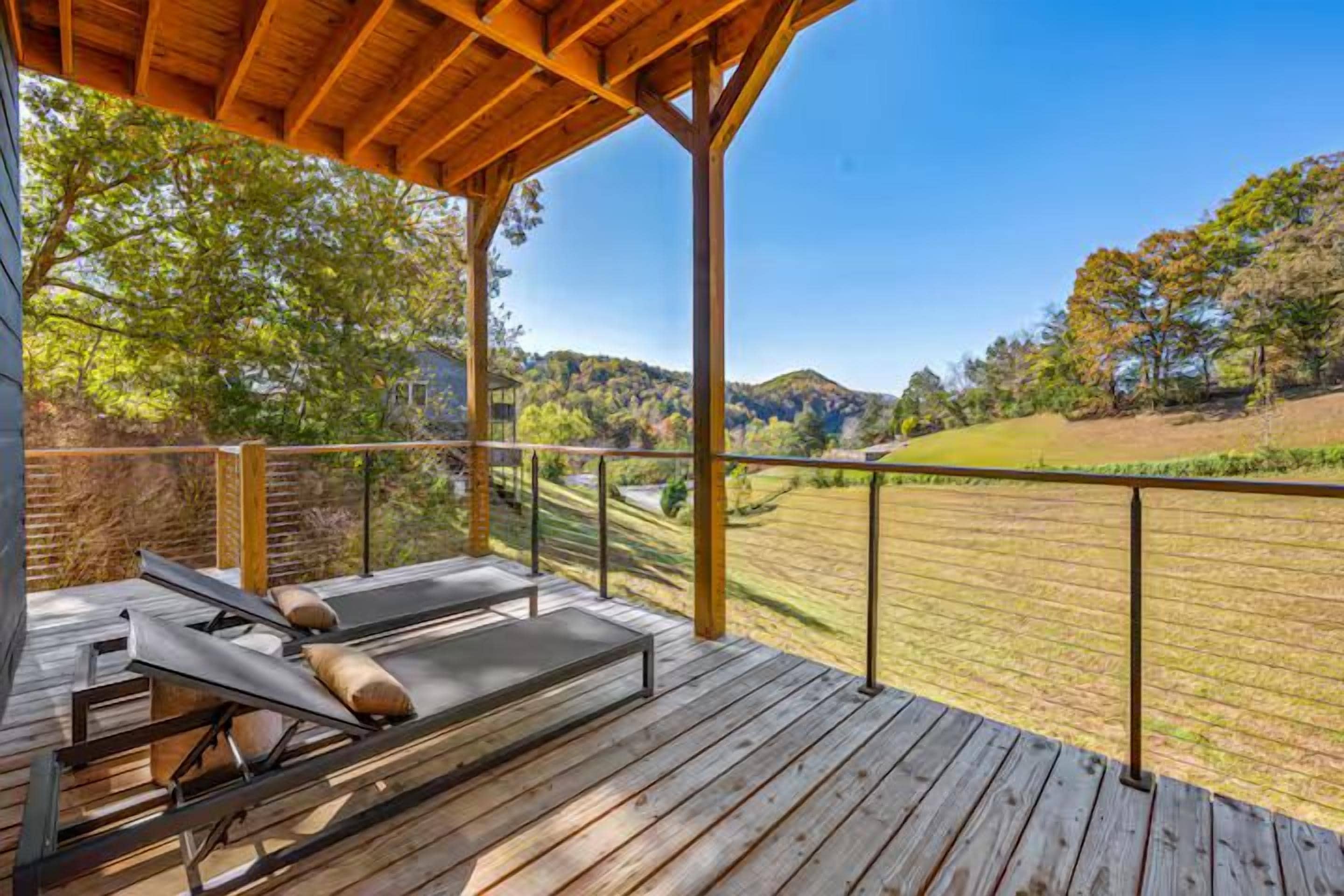 Une terrasse en bois avec un espace détente, une vue sur un paysage verdoyant et un ciel dégagé.