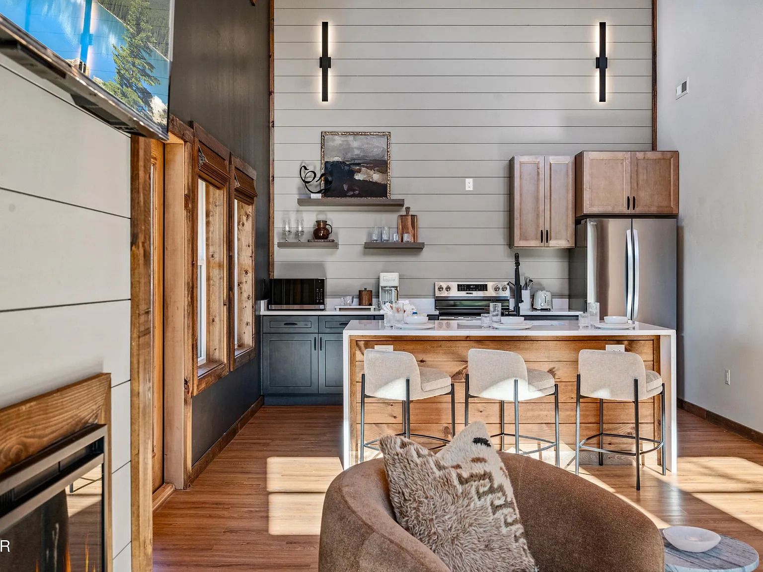 A modern kitchen with a central island, bar stools, and a rustic wooden accent wall.