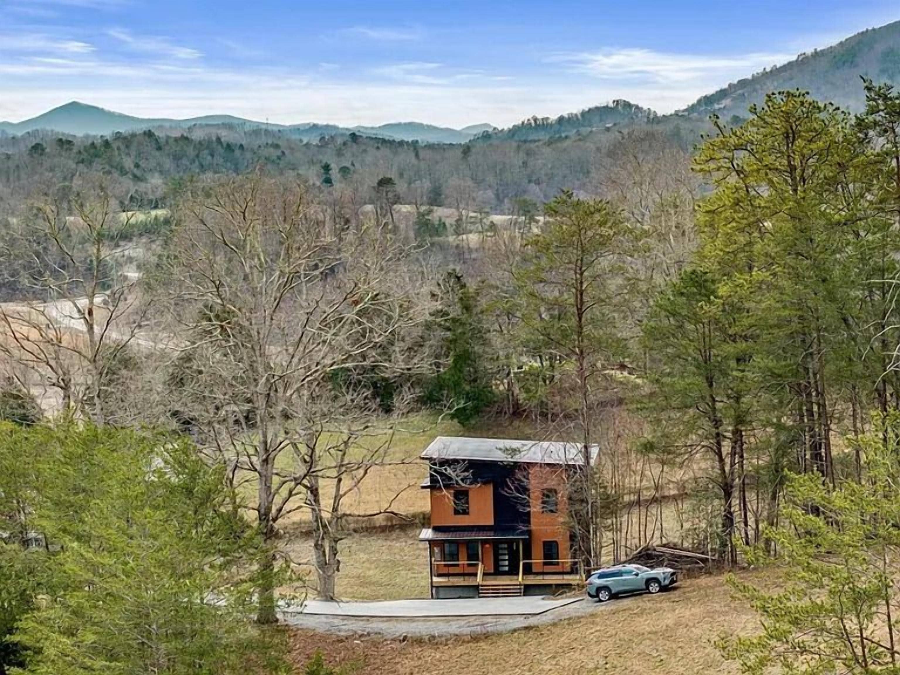 A cabin with a sloped roof, surrounded by trees and a mountain backdrop.