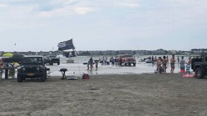 A beach with people, vehicles, and a flag.