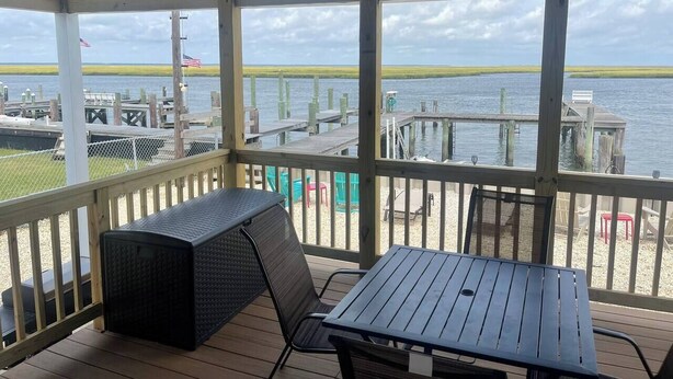 A covered outdoor area with a table and chairs, overlooking a body of water with docks and boats.