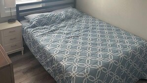 A bedroom with a bed, a nightstand, a lamp, and a window with blinds.