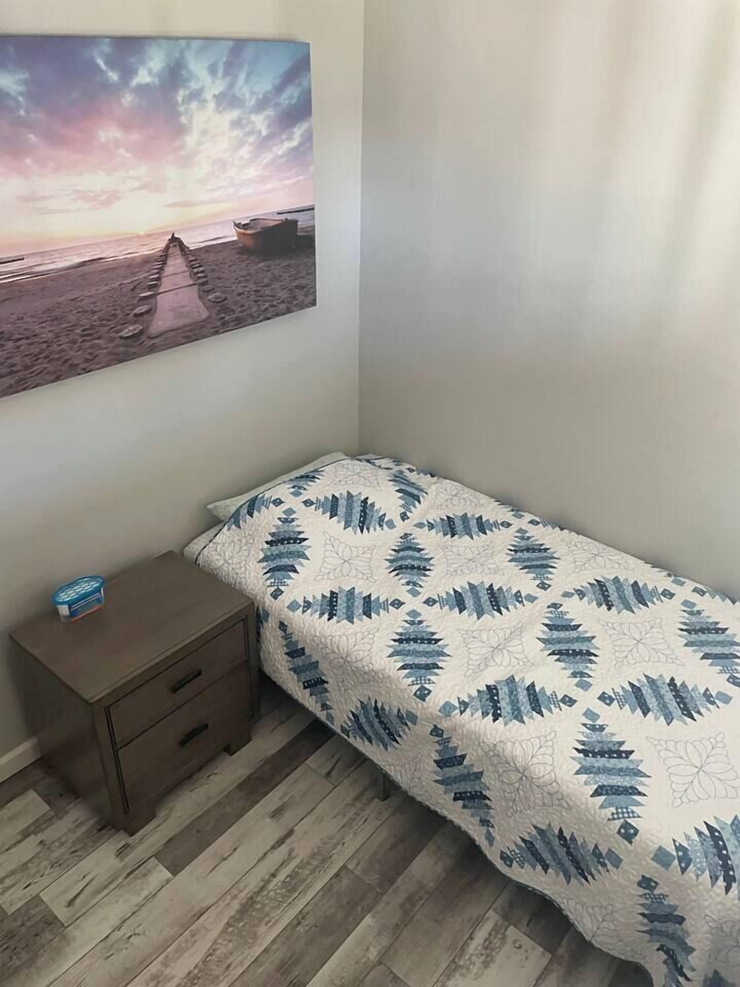 Un dormitorio con una cama, una mesita de noche y un cuadro colgado en la pared.
