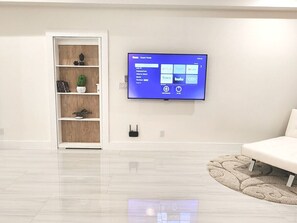 Ein modernes Wohnzimmer mit flachbildfernseher an der Wand, einem weißen Sofa und einem Bücherregal aus Holz.