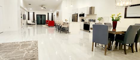 A modern kitchen with white cabinets, a central island, and a dining area with a red chair and grey chairs.