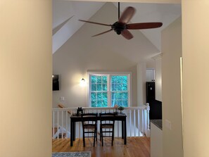 Ein Essbereich mit Tisch und Stühlen, einem Deckenventilator, einem Fenster mit Blick auf Bäume und einer Treppe, die zu einer anderen Ebene führt.