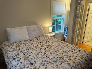 Ein Schlafzimmer mit Bett, Nachttisch, Fenster und Tür.