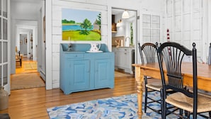 A dining area with a wooden table and chairs, a blue cabinet, and a painting on the wall. - Pom Cottage - 3BR Waterfront Cottage Near Acadia (Prospect Harbor)