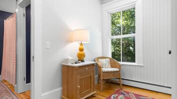 A room with a wooden cabinet, a wicker chair, a patterned rug, and a window with a view of trees.