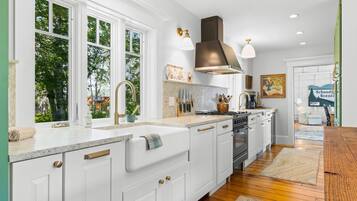 A modern kitchen with white cabinetry, a large island, a stove, and a window overlooking greenery.