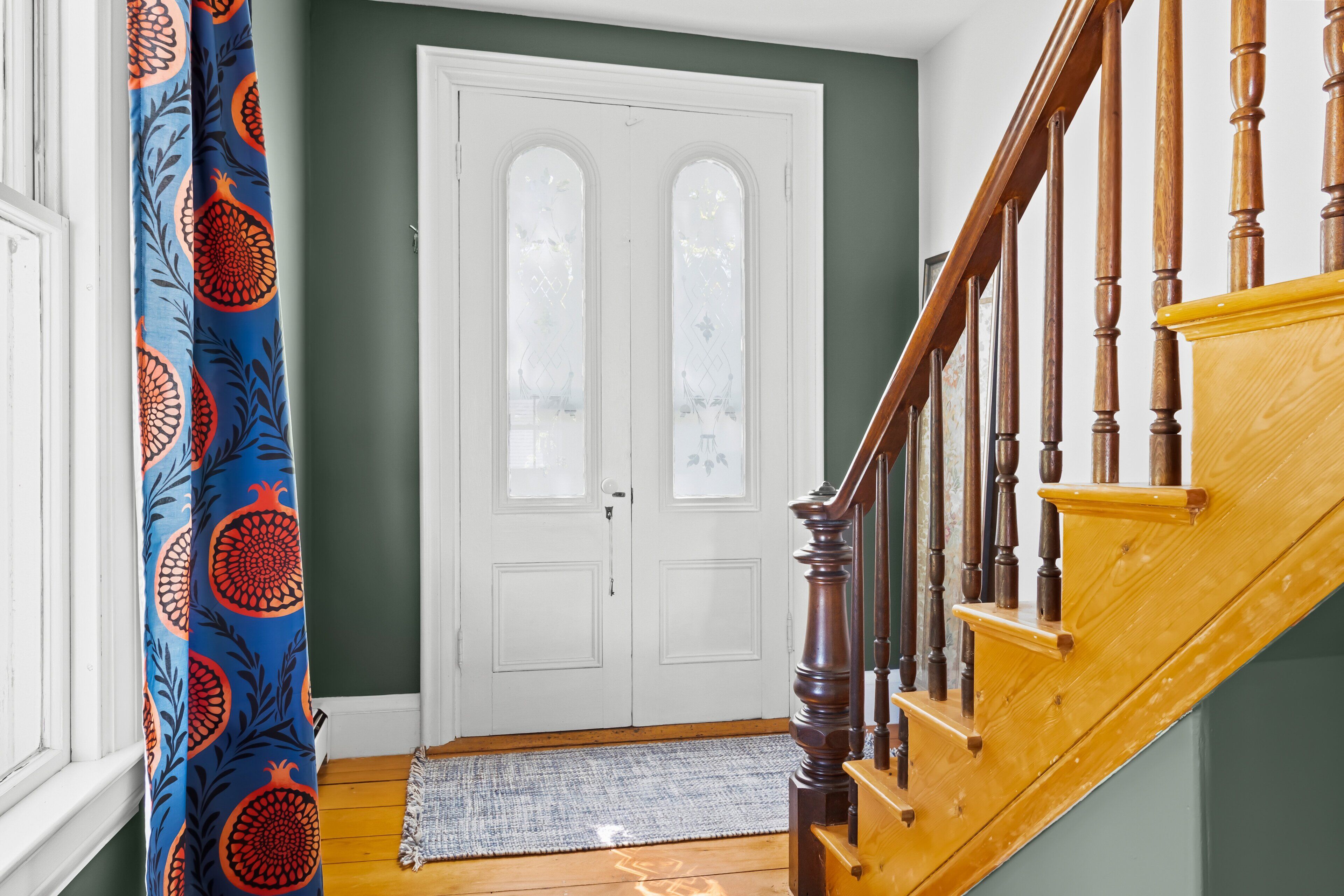 A staircase with wooden balusters, a white door with glass panels, and a blue curtain with a pomegranate pattern.