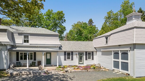 A two-story house with a front porch, a green door, and a gravel driveway. - Pom Cottage - 3BR Waterfront Cottage Near Acadia (Prospect Harbor)