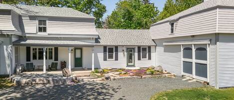 A two-story house with a front porch, a green door, and a gravel driveway.