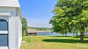 A house with a grassy yard, a small shed, and a body of water in the background. - Pom Cottage - 3BR Waterfront Cottage Near Acadia (Prospect Harbor)