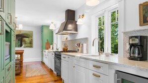 A modern kitchen with white cabinets, a stove, and a coffee maker. - Pom Cottage - 3BR Waterfront Cottage Near Acadia (Prospect Harbor)