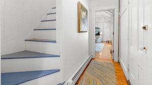 A staircase with blue steps, a framed picture on the wall, and a wooden floor leading to a room with a door. - Pom Cottage - 3BR Waterfront Cottage Near Acadia (Prospect Harbor)