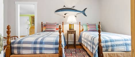 A bedroom with two beds, a patterned rug, a wall-mounted fish decoration, and a bedside lamp.