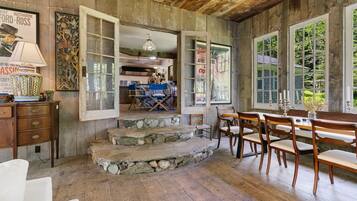 A rustic interior with stone steps leading to a dining area, wooden furniture, and a view of the outdoors.