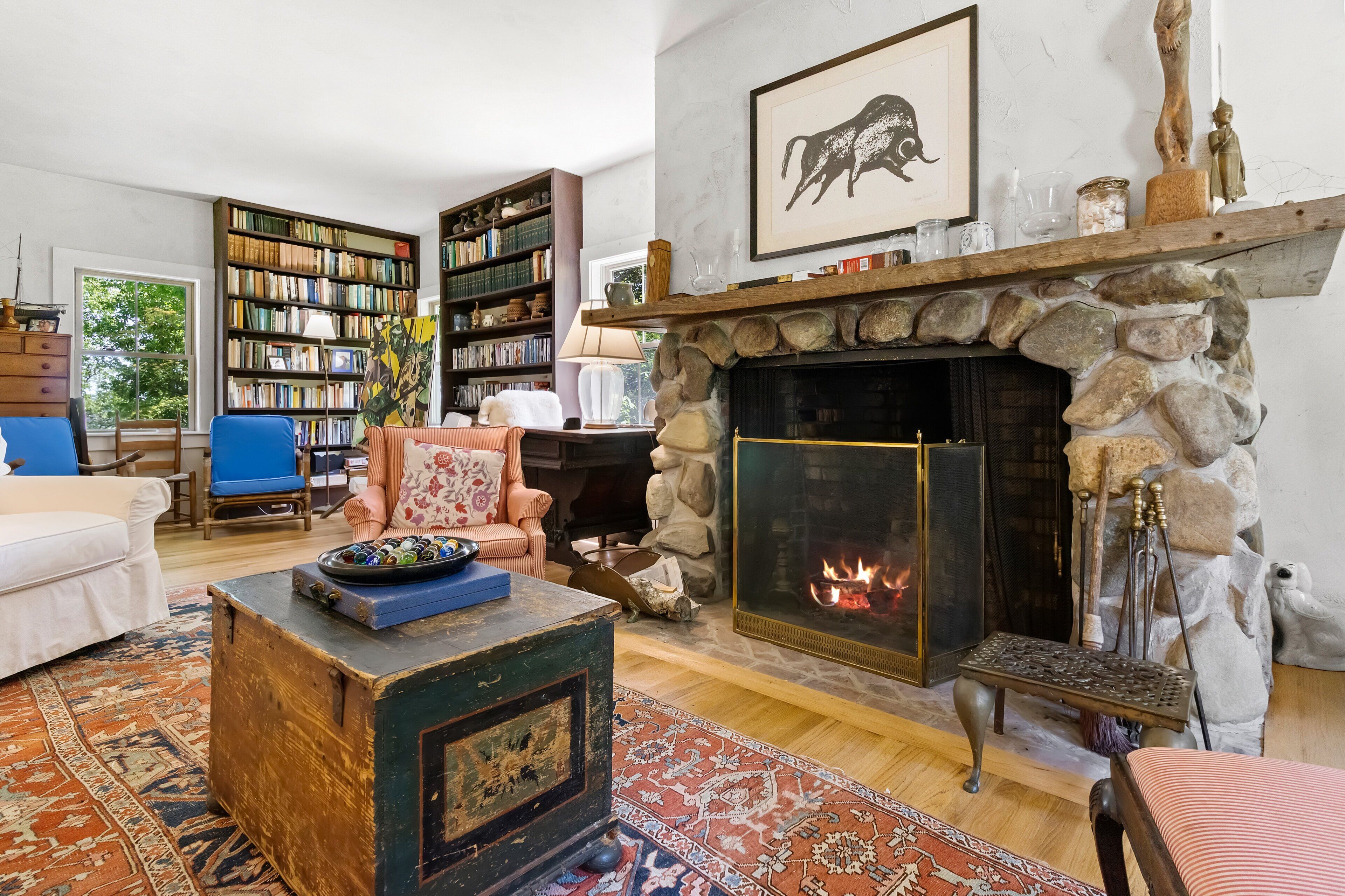 Ein gemütliches Wohnzimmer mit Kamin aus Stein, einer Bücherwand, einem gemusterten Teppich und einer komfortablen Sitzecke.